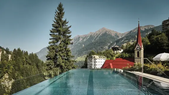 Outdoor pool with a view of a church and mountains in the background.