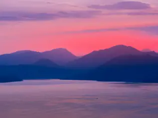 A calm lake with distant mountains under a cloudy sky.