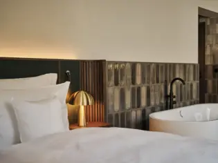 A hotel room in which a free-standing bathtub stands next to a bed with white bed linen.