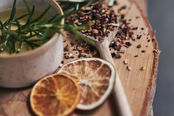 A bowl of liquid with rosemary and spices on a wooden surface.