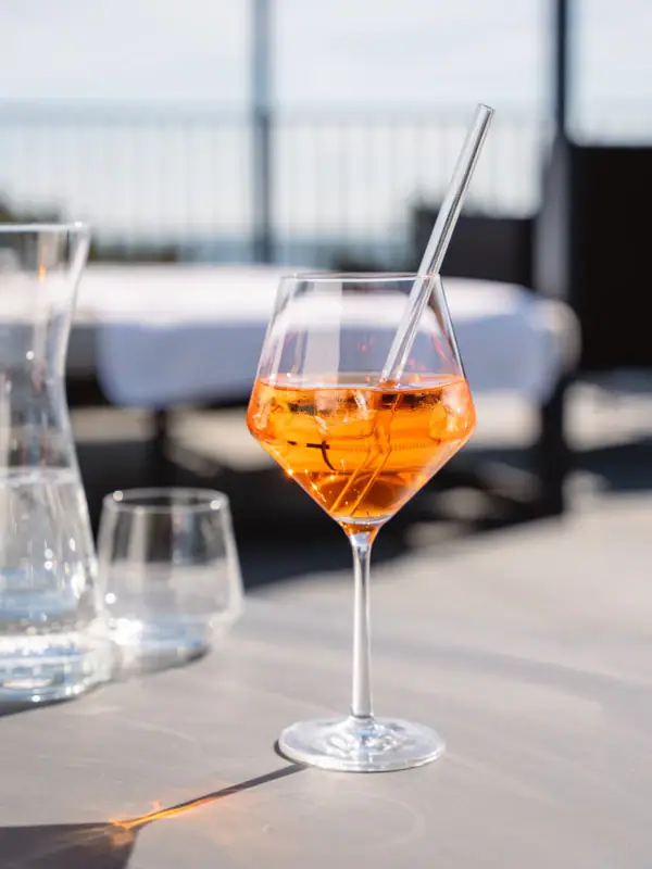 A glass with an orange cocktail in it.