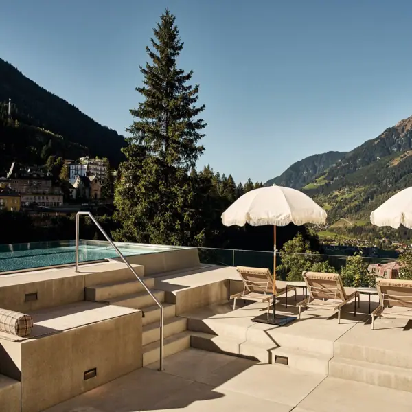 The outdoor pool at SPA-ROSA Bad Gastein, with parasols and sun loungers on a sunny day.