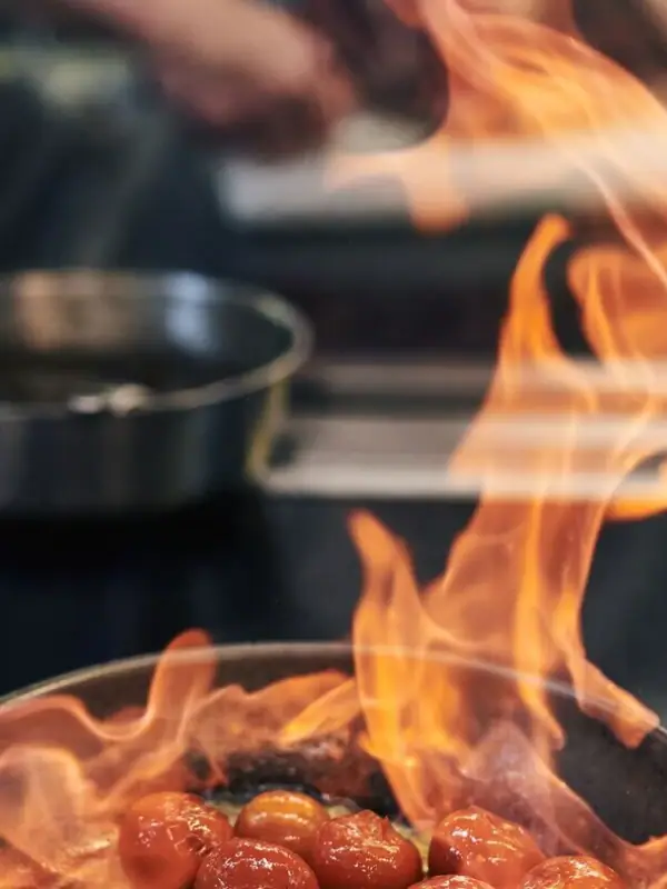 A pan with food on fire, featuring sizzling meat.
