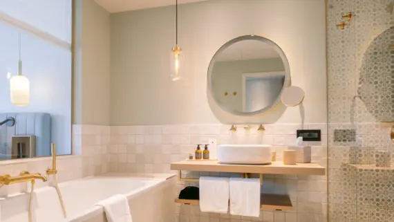 Elegant bathroom featuring a round mirror above a sink and a tub, complemented by tiled walls.