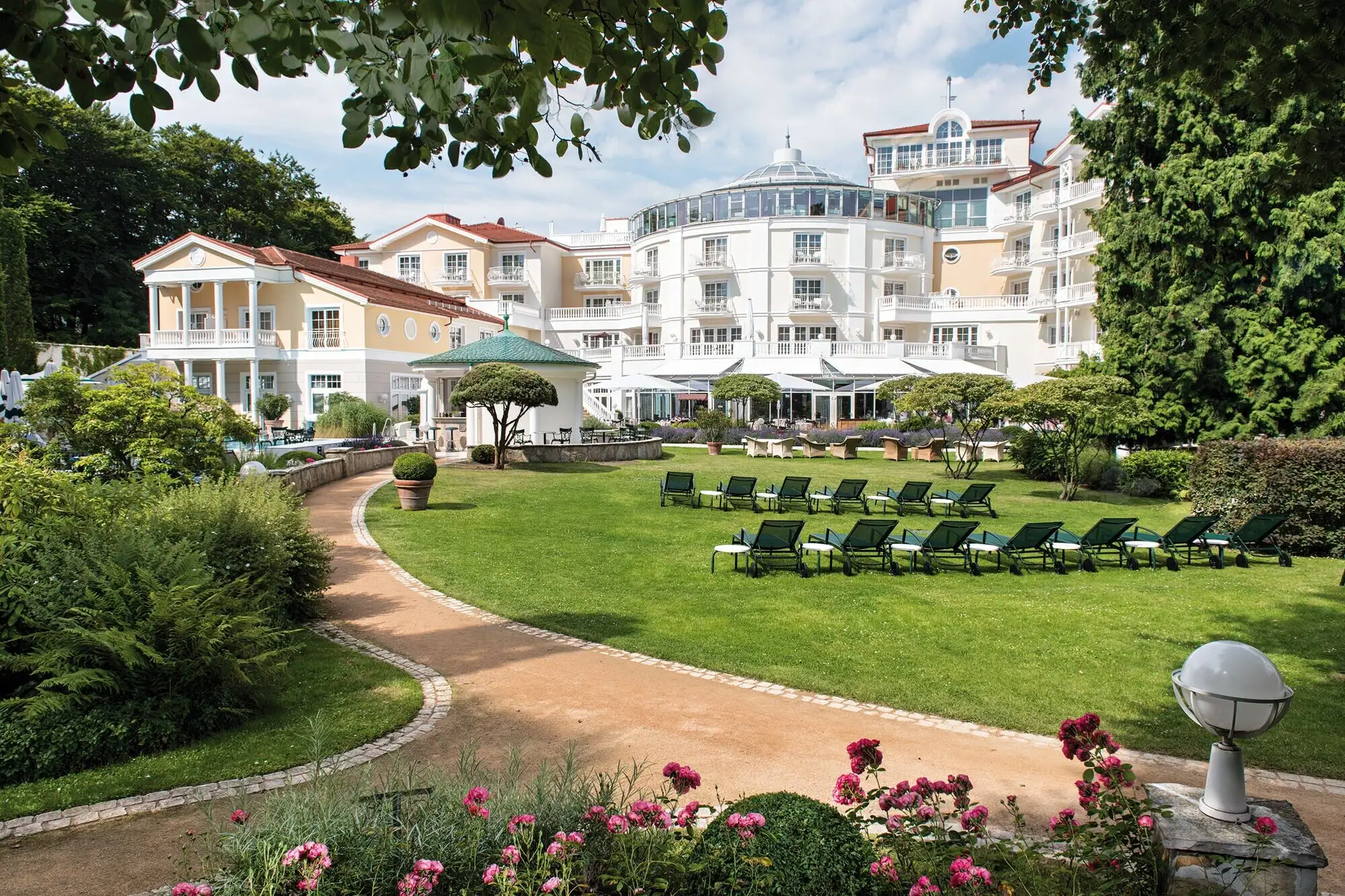 Strandidyll Heringsdorf Liegestühle im Garten mit Rasen und einem Hotel sowie Bäumen im Hintergrund.