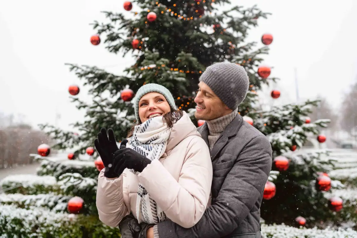 A man and a woman are standing in front of a Christmas tree.