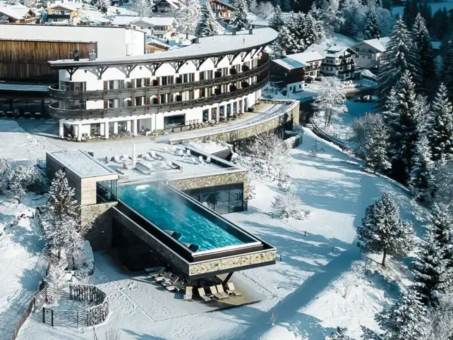 Building with infinity pool in the snow, surrounded by trees and winter landscape.