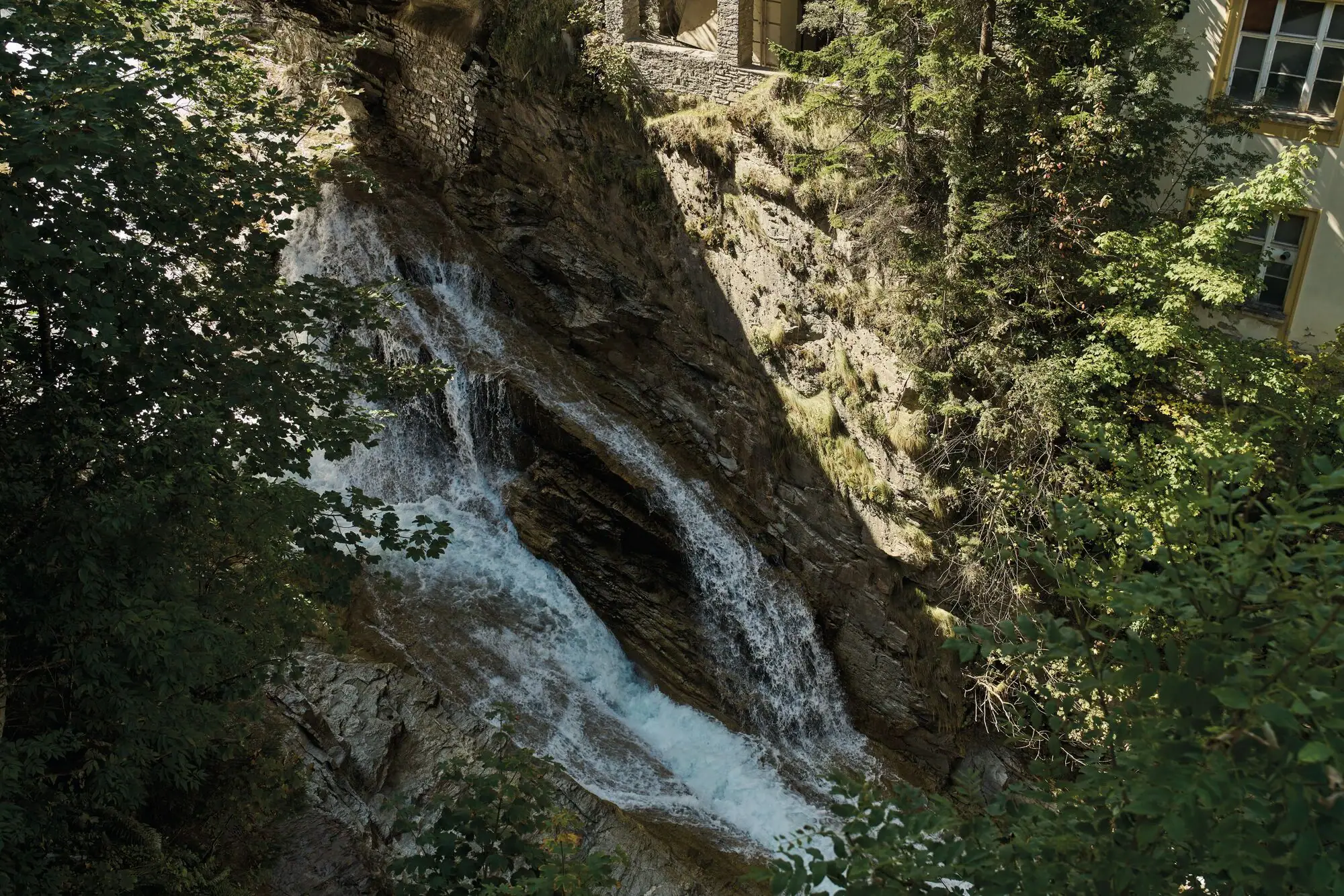 Waterfall cascading down a cliff surrounded by trees and lush greenery.
