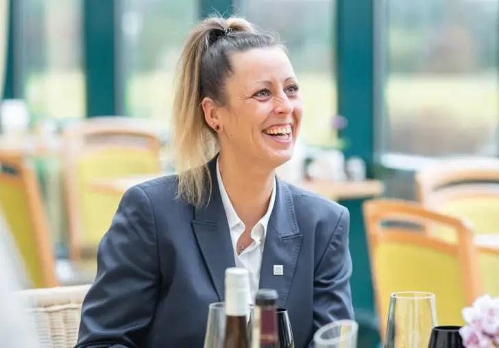 Woman smiling at a table with wine glasses.