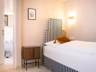 Bed with a striped headboard, crisp linens, and a nightstand in a well-appointed room.