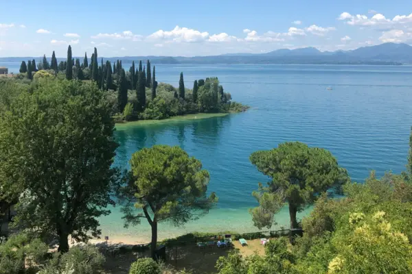 The clear Lake Garda with trees under a cloudy sky.