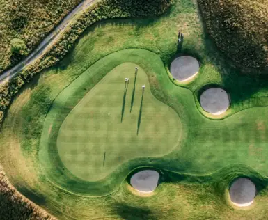 Golf course with sand bunkers and people on the green from a bird's eye view.