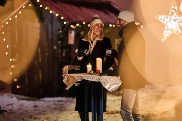 A man and woman standing outside holding candles surrounded by festive lights.