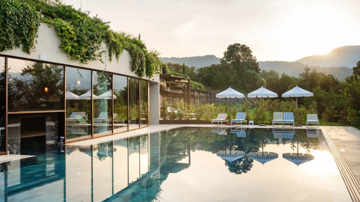 A swimming pool with sun loungers and parasols in front of a building.