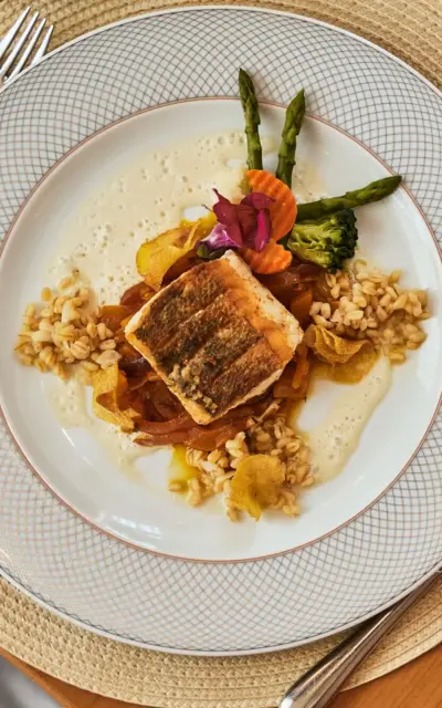 A hand holding a glass of wine beside a plate of food on a table.