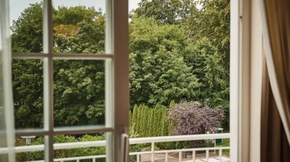 View through a window of trees and a building in daylight.