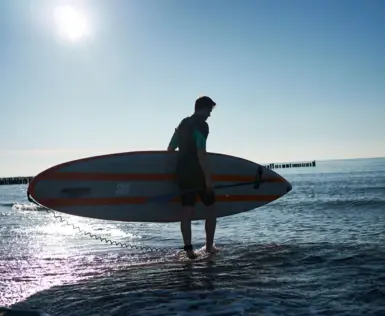 Man carrying a surfboard in the water.