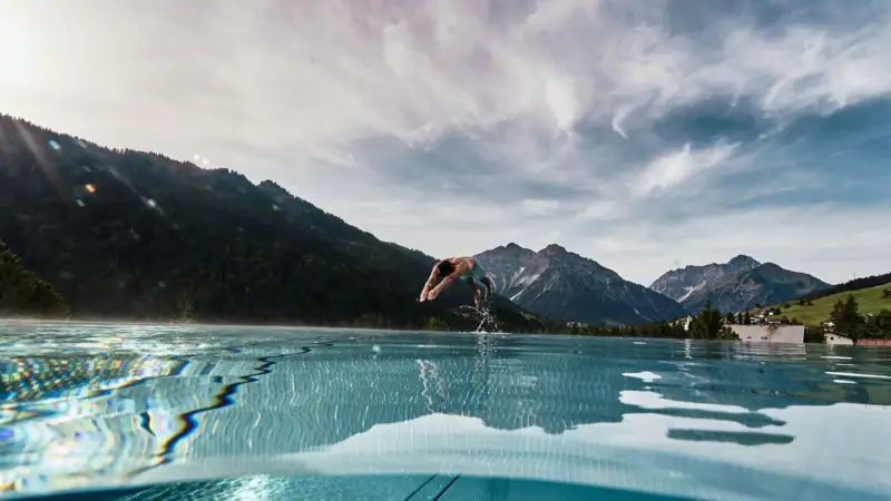 A person jumping into a swimming pool with mountains in the background.