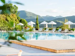 Outdoor pool surrounded by sun loungers, umbrellas and trees.