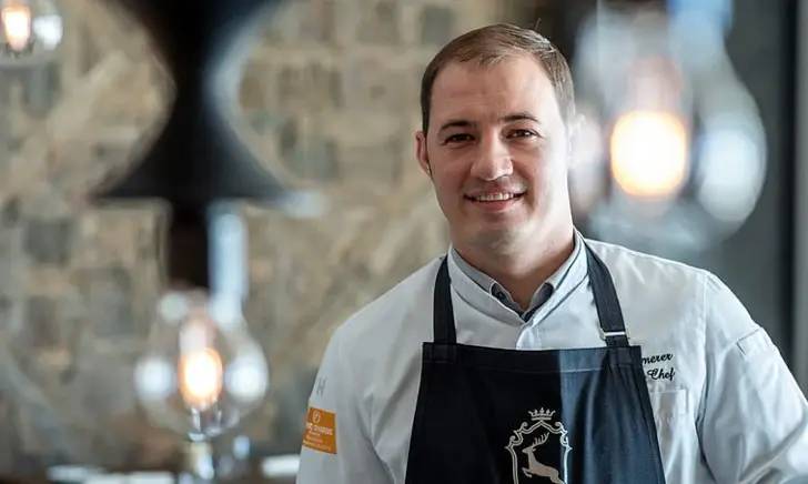 Man in black apron smiling in a restaurant.