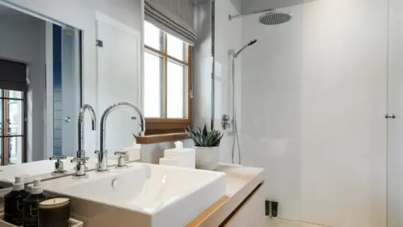 A modern bathroom with an angular washbasin on a wooden washstand and a glazed shower cubicle in the background. 