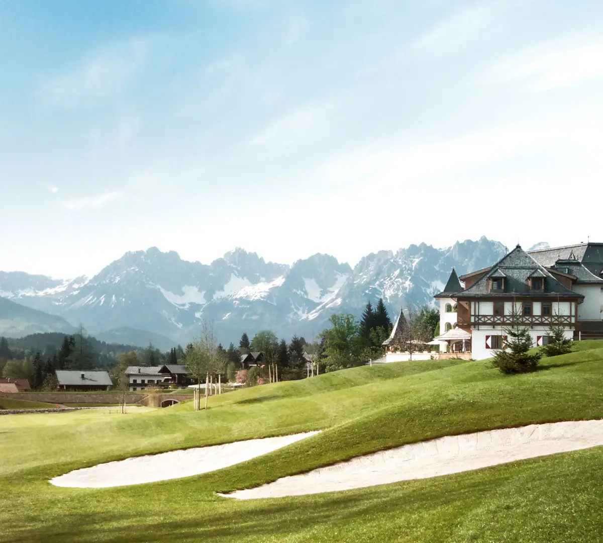 Golfplatz mit Haus und Bergen im Hintergrund