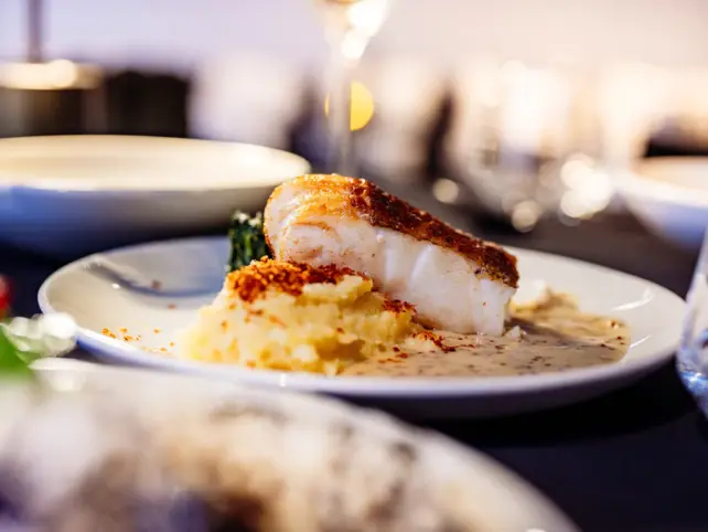 A plate of fish on a bed of mashed potato and sauce, served on a table in a restaurant setting.