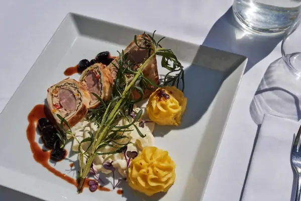 A plate of cuisine with a fork and wine glass on a table.