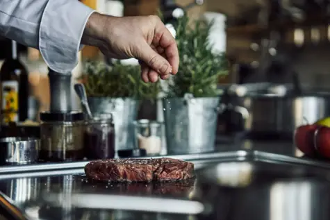 A hand sprinkling salt on a piece of meat.