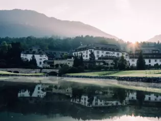 A building beside a lake with trees, mountains, and a clear sky reflected in the water.