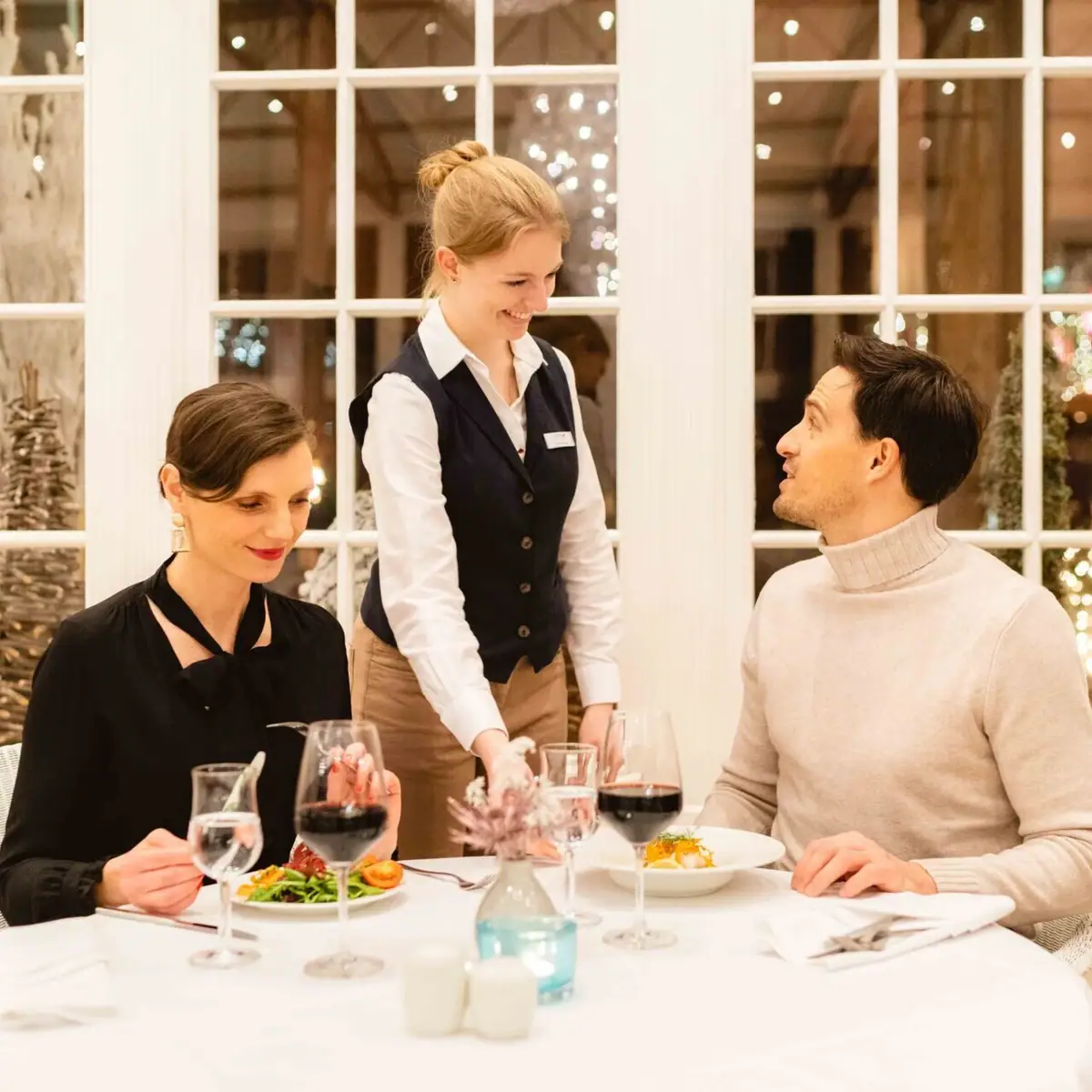 Christmas with A-ROSA A group of people sitting at a table indoors with tableware and wine glasses.