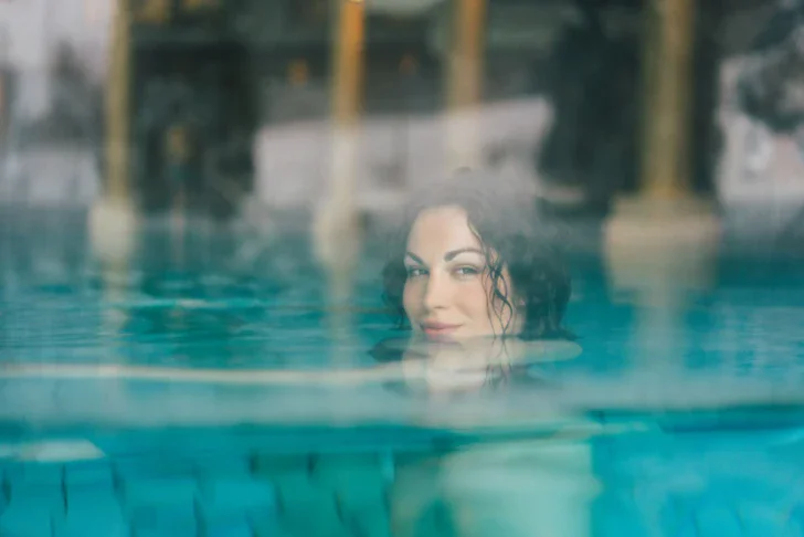 A woman is swimming in the warm, steaming water of a pool, only her head above the surface. 