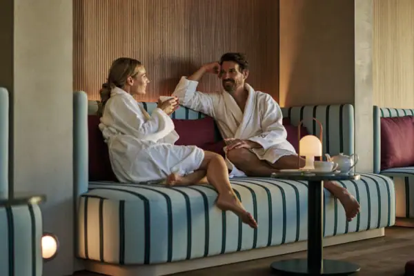 A man and woman in bathrobes sitting on a couch indoors.
