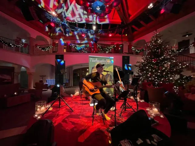 A hotel entrance hall decorated for Christmas, with a small red stage in the centre on which a musician is performing. 