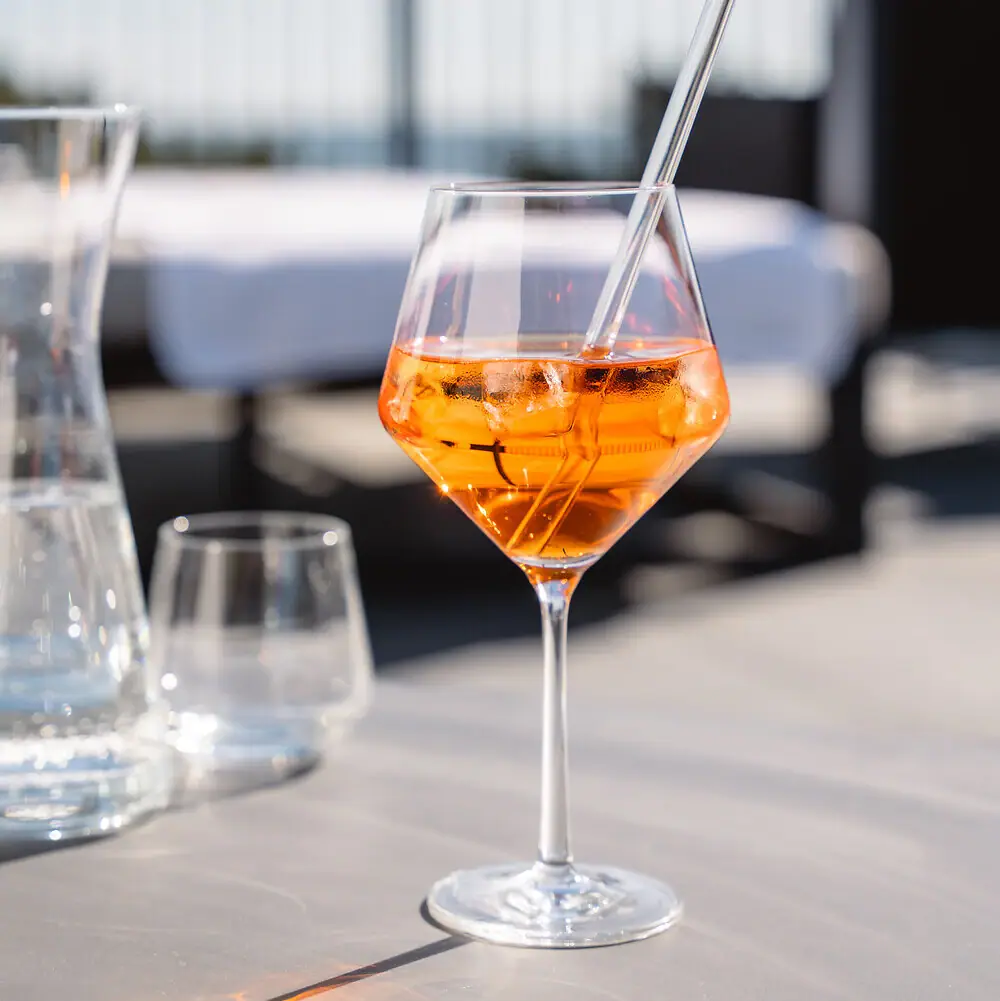 A glass of orange cocktail with ice on a table.
