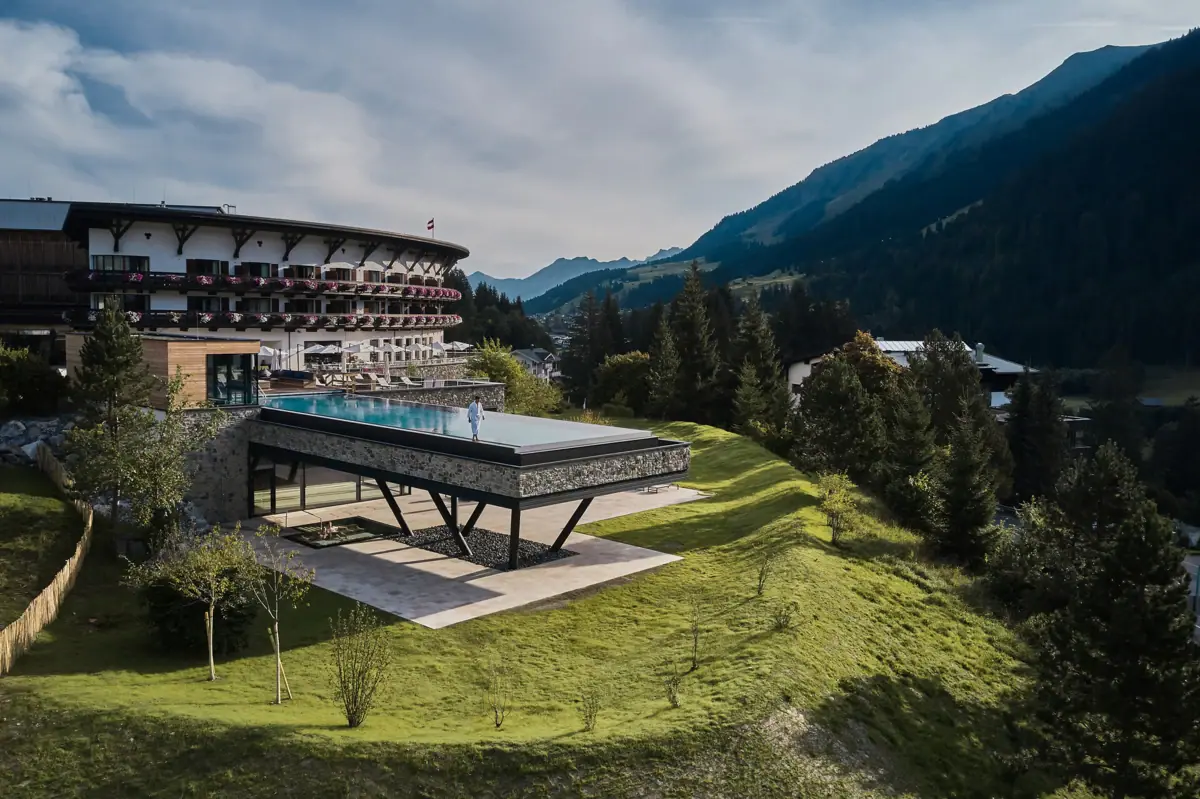 A building with a swimming pool in the middle, surrounded by mountains and blue skies.