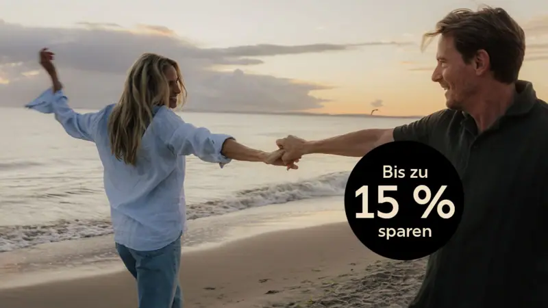 A man and woman holding hands on a beach at sunset.