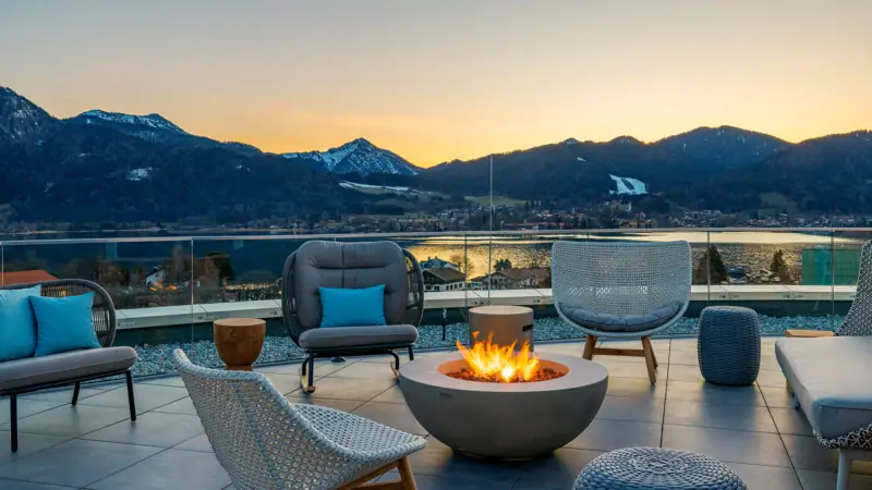 A fire pit surrounded by chairs with a view of mountains and water.